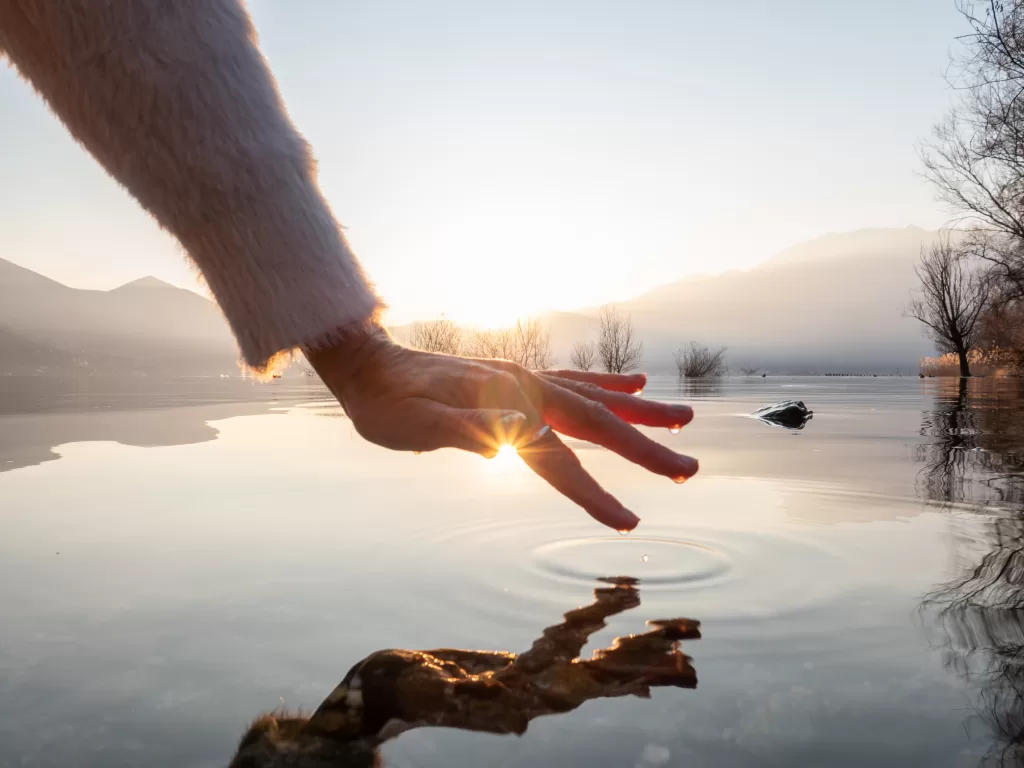Detail of hand touching and caressing water surface of beautiful lake at sunset, mountain view. Purity freshness clean concept, one person touching lake with hand
